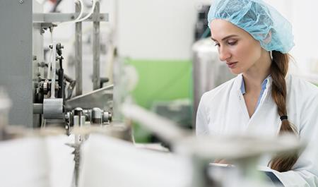韦德注册平台 Industry - Happy female employee wearing protective headwear and white lab coat while working as a manufacturing engineer in a contemporary factory
