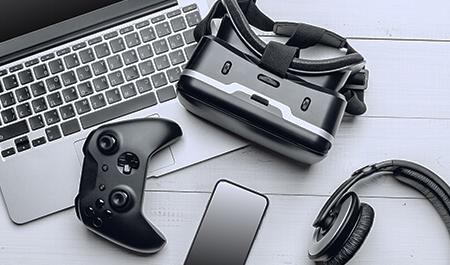 Laptop, headphones, cell phone, gaming controller and AR goggles displayed on a tabletop