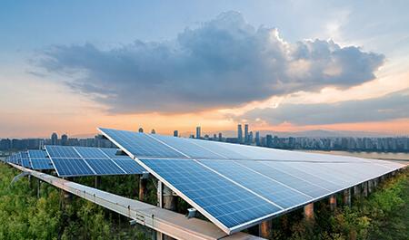 Solar panels facing sky at sunset with a city skyline in the background